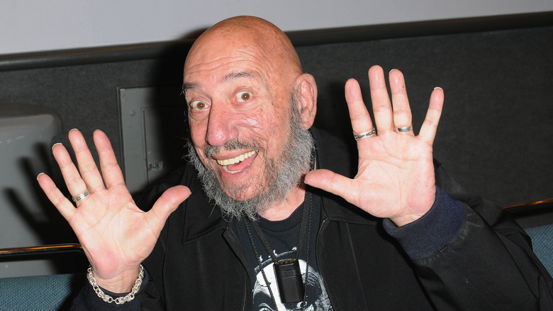 Sid Haig raises his hands and grins 