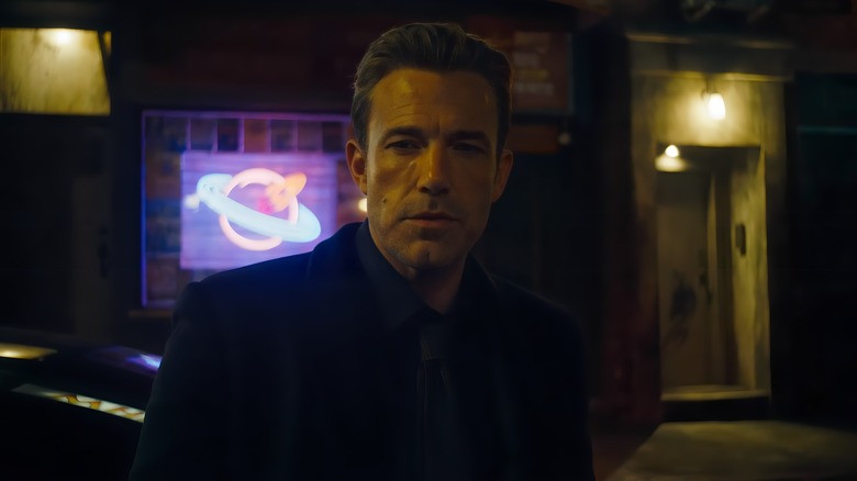 Bruce Wayne stands in front of a neon sign