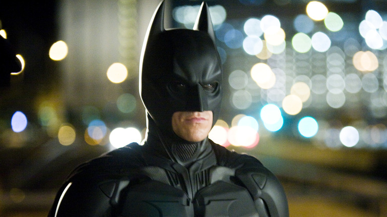 Batman wearing mask and suit city behind him