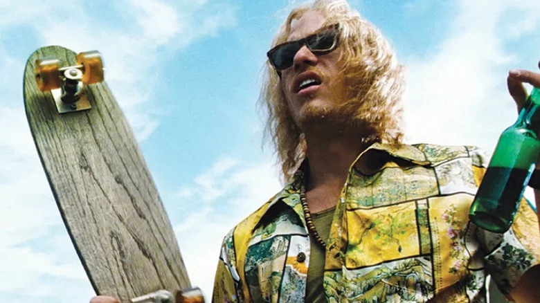 Blonde Ledger in sunglasses holding skateboard and beer