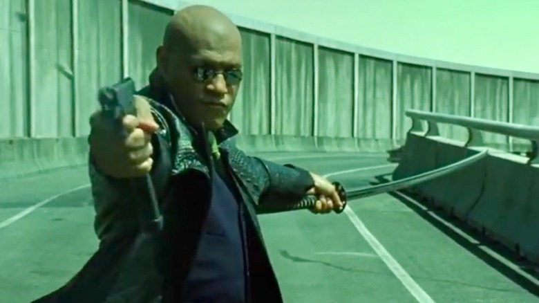 Morpheus fires a gun while holding a sword