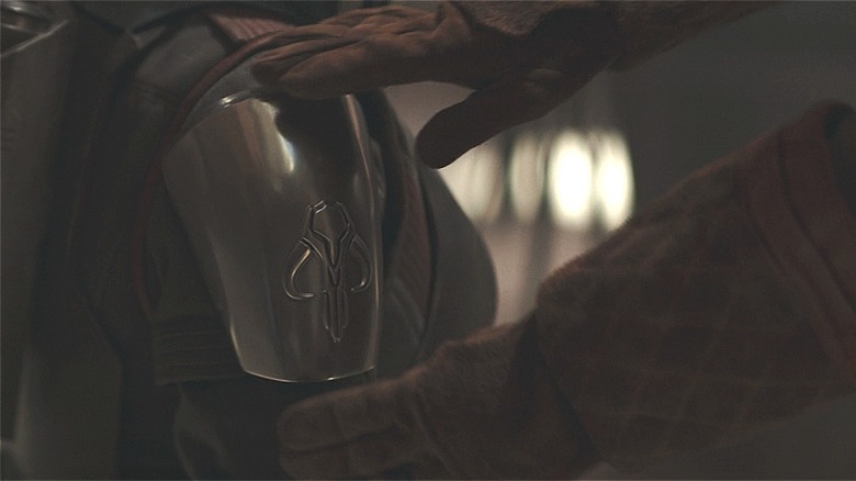 The Armorer placing the mythosaur pauldron on the arm of Bo-Katan's armor