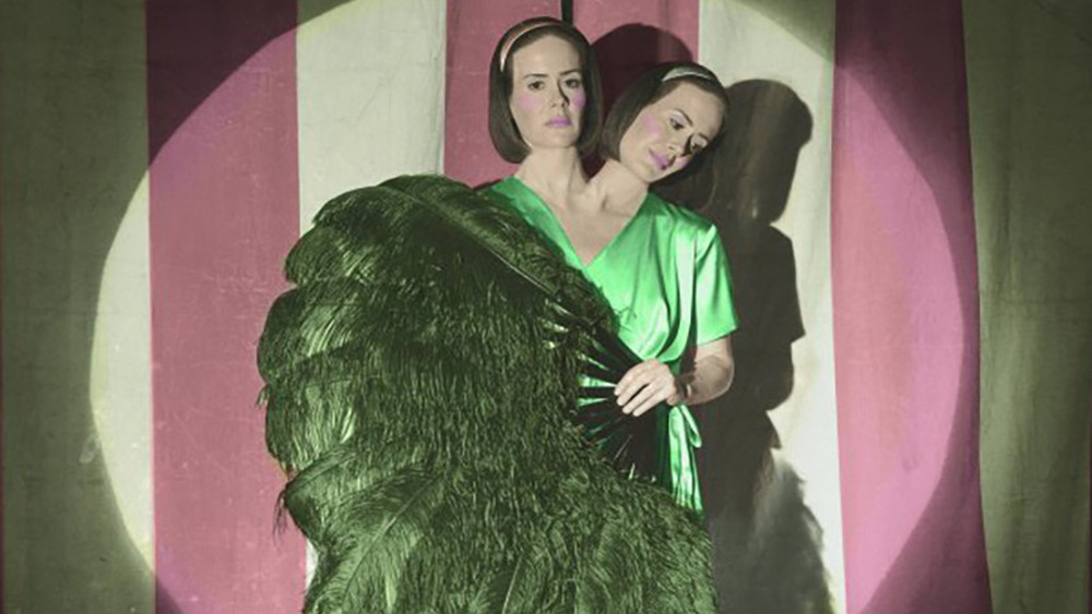 Conjoined twins standing on stage with a large feather