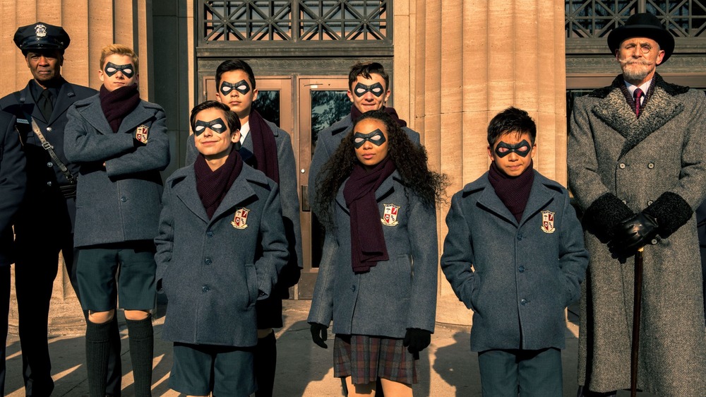 Reginald Hargreeves posing with The Umbrella Academy superheroes
