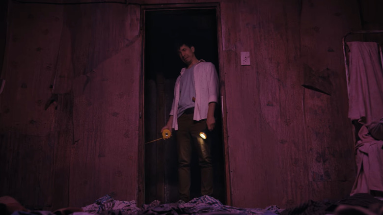 AJ (Justin Long) holds measuring tape and flashlight in basement door