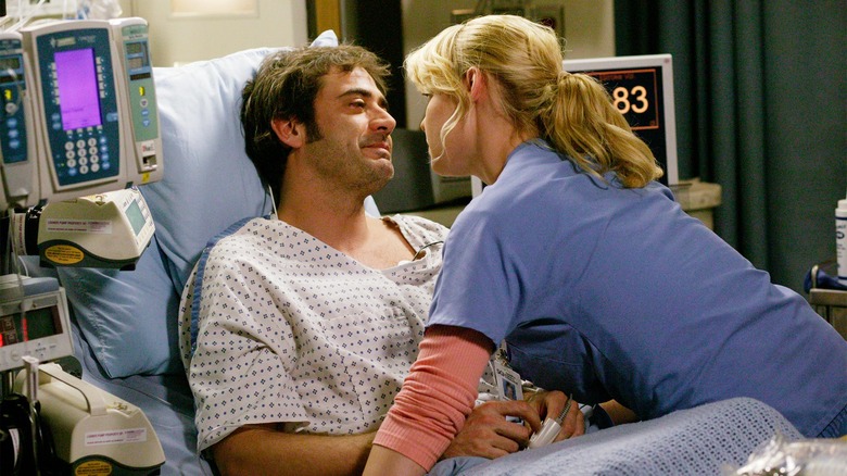 Izzie leans over Denny in bed