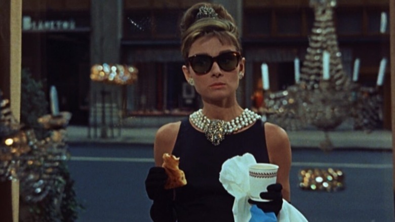 Holly Golightly holds coffee and croissant