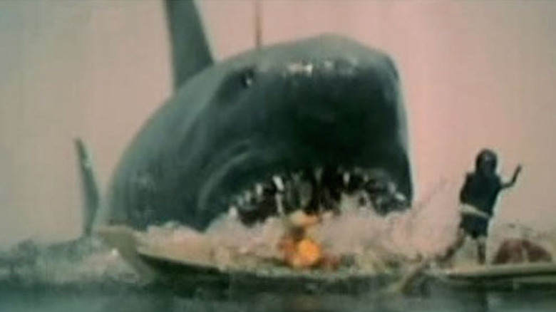 A giant shark attacks a model of a boat and its passenger