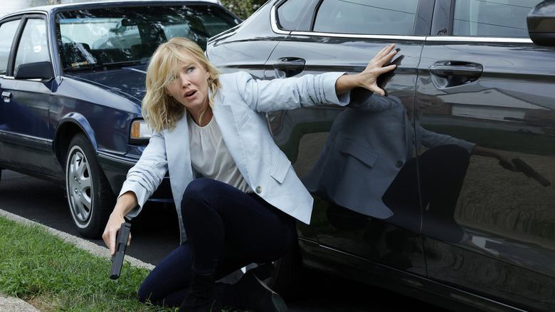 Rollins crouching by a car with a gun