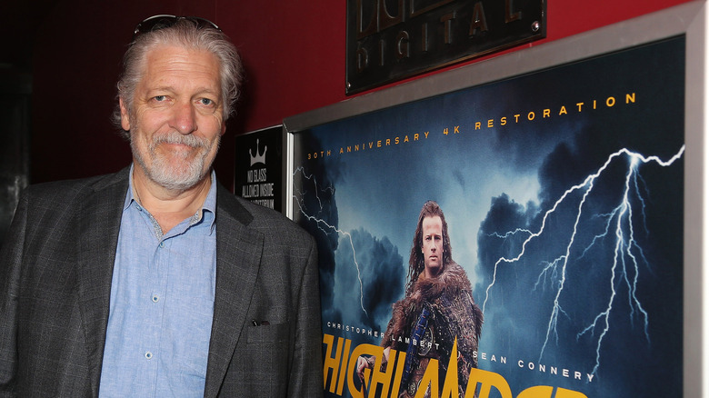 Clancy Brown posing in front of a Highlander poster