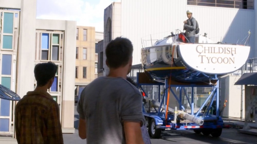 Danny Pudi as Abed and Joel McHale as Jeff watch Donald Glover as Troy ride out on yacht Childish Tycoon (on the back of a truck) in Community