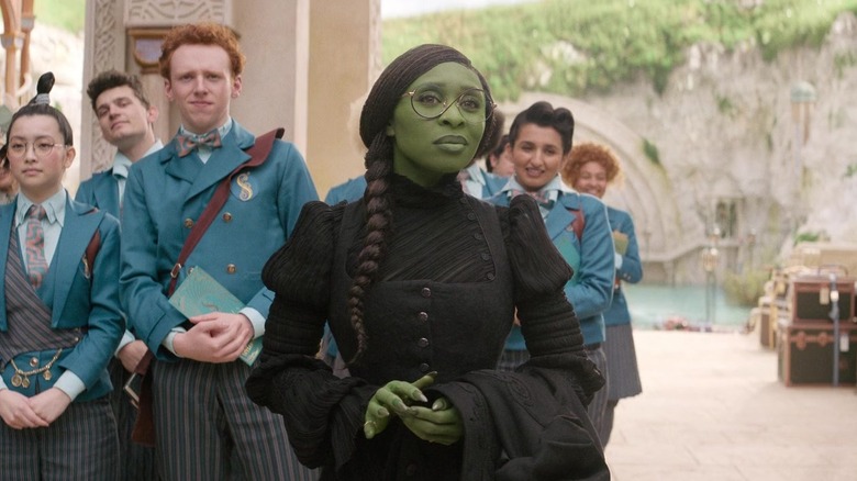 Elphaba standing by other students looking at professor