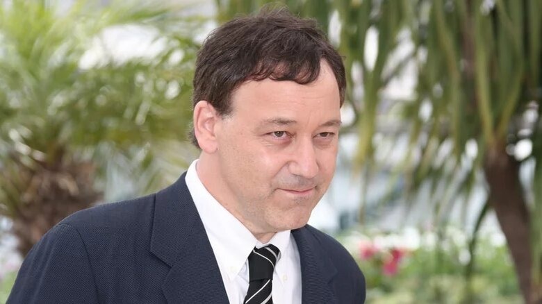 Sam Raimi stands in front of green leaves
