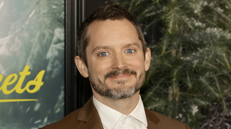 Elijah Wood smiling wearing brown suit