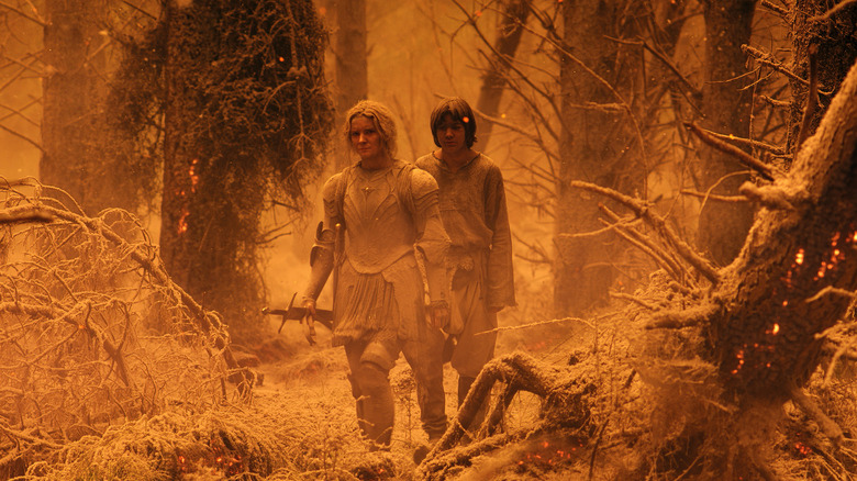 Galadriel and Theo walk through ash-covered forest