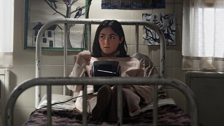 Leena sits on her bed in an institution, looking nervously to the side