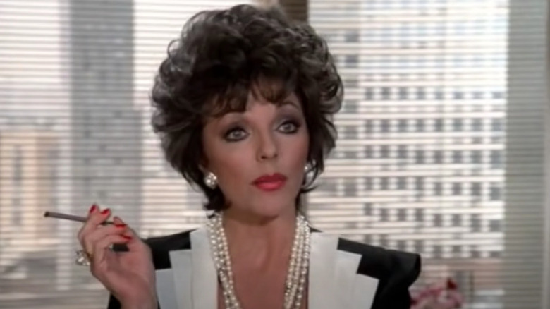 Alexis Carrington holds cigarette by window 