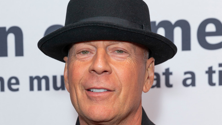 Bruce Willis smiling with a pork pie hat on