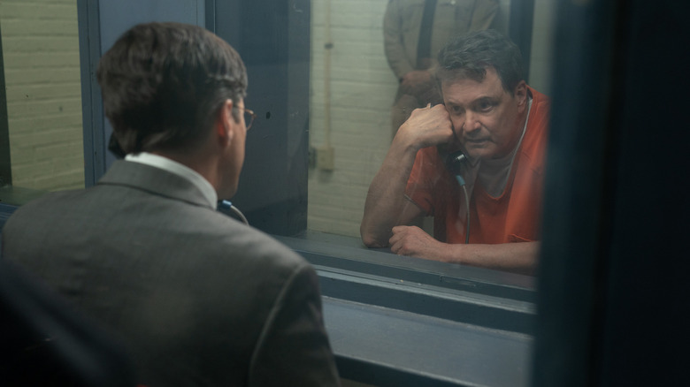 Michael in a prison jumpsuit talking to a man through a prison window with a telephone
