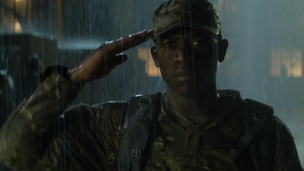 Damson Idris as Harp salutes in the rain