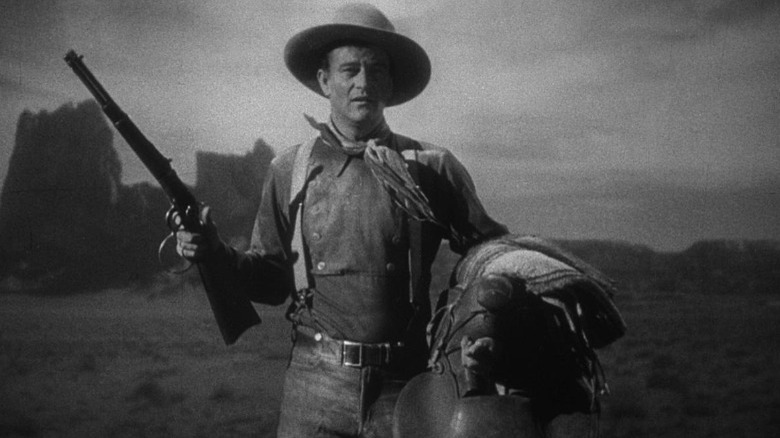 John Wayne holds saddle and gun