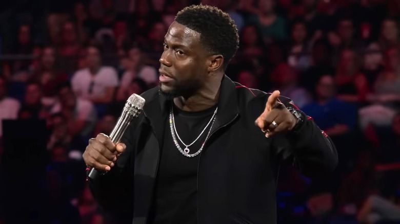 Kevin Hart in a black outfit doing standup with a crowd behind him