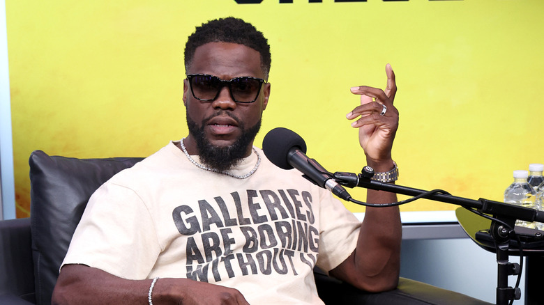 Kevin Hart wearing sunglasses speaking on a podcast in 2024