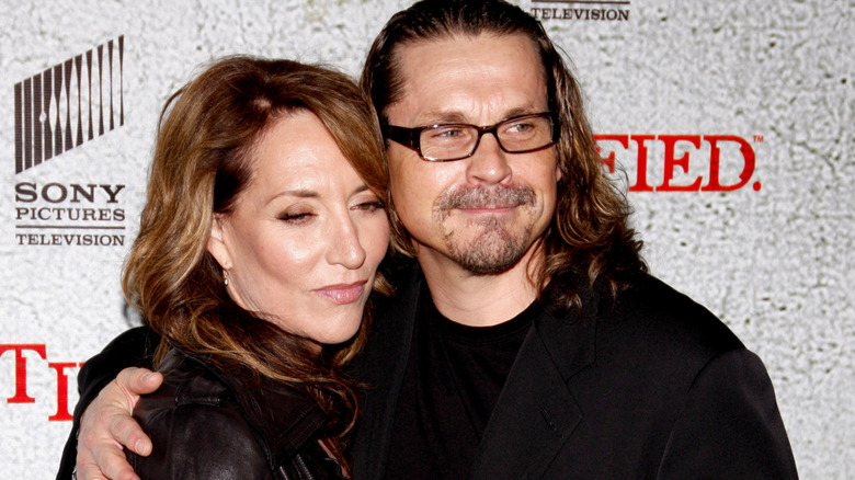 Katey Sagal standing close to Kurt Sutter, both wearing black, in front of grey background