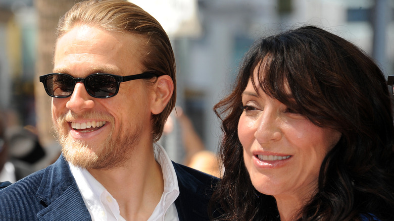 Charlie Hunnam wearing sunglasses smiling next to Katey Sagal smiling