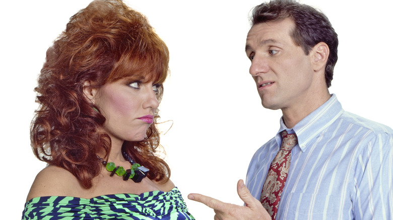 Peggy Bundy pouting at Al Bundy, who is pointing at her, in front of white background