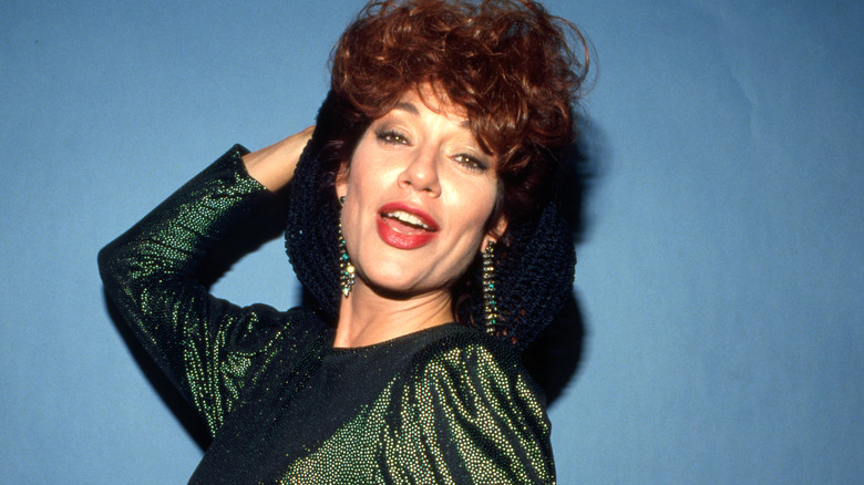 Katey Sagal posing with hand behind her head in front of a blue background