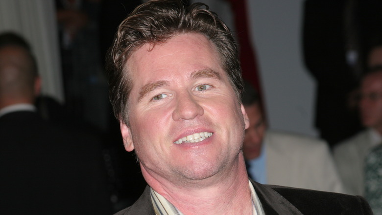 Val Kilmer smiling at an event with people in the background