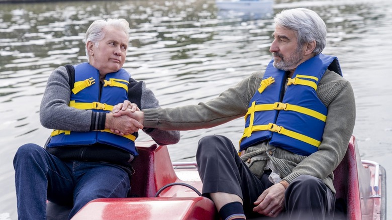 Robert and Sol hold hands while paddling a paddle boat on a body of water