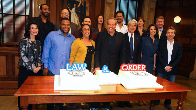 Sam Waterston, Dick Wolf, and the Law & Order cast gather around celebratory Law & Order-themed cakes in a courtroom set