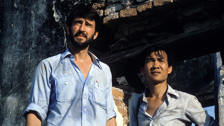 Sydney and Dith stand in front of a dilapidated building, looking off to the horizon