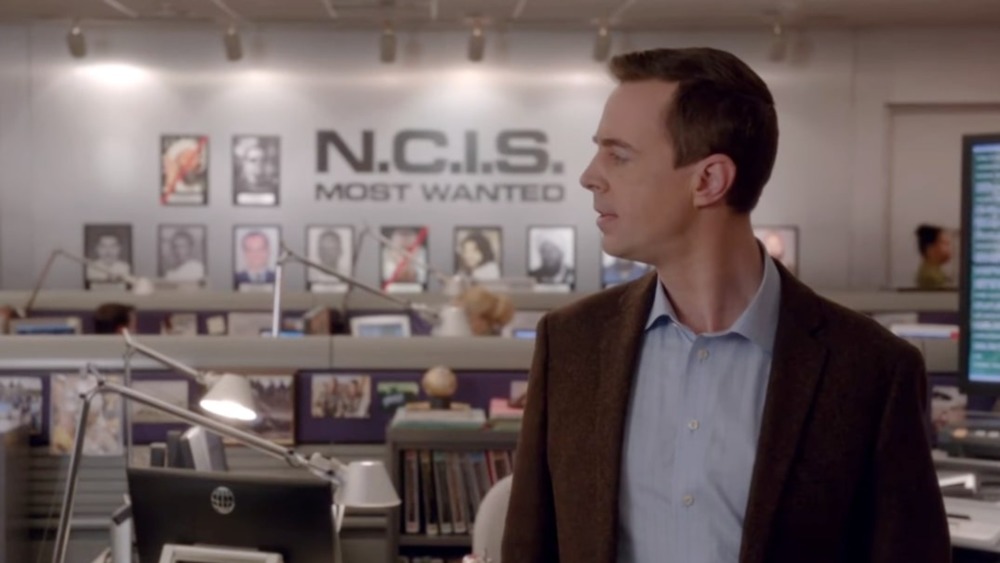 McGee stands in front of the most wanted wall on NCIS