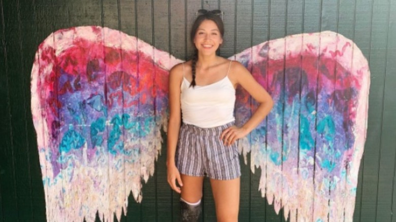 Alaqua Cox standing in front of painting of wings