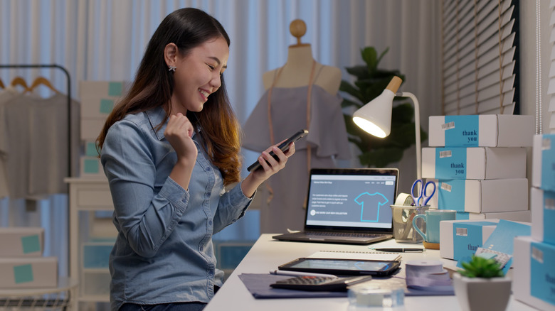 A woman sits at a desk working on her phone