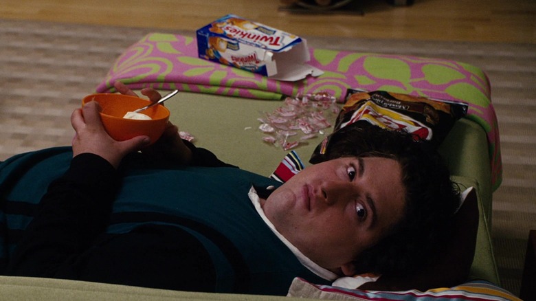 Teenage Ben laying on a snack wrapper-covered couch while eating a bowl of ice cream