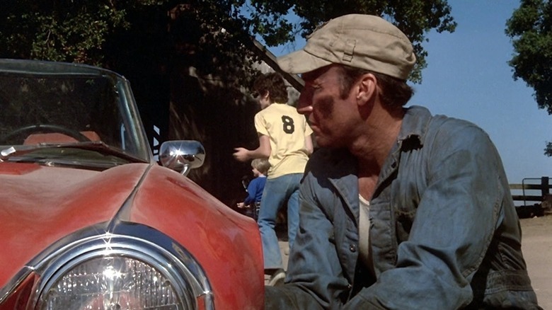 Ed Lauter kneels next to car