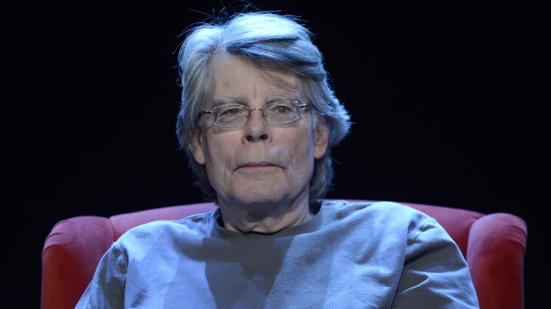 Stephen King serious sits in chair