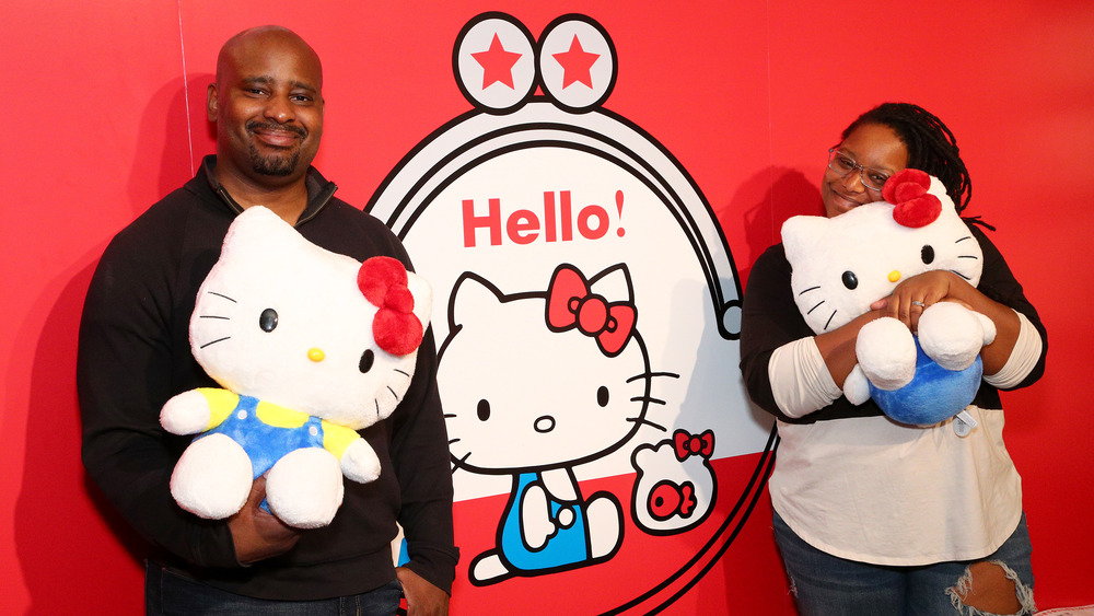 People stand in front of an image of the original Hello Kitty coin purse