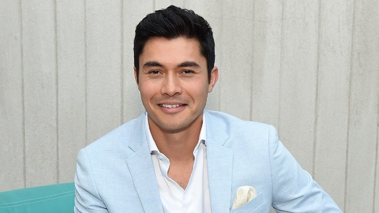 Henry Golding smiling in chair