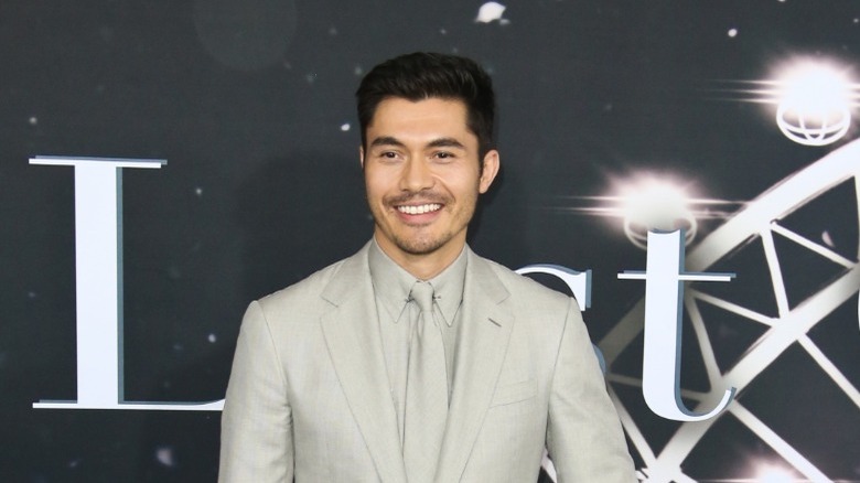 Henry Golding smiling in suit while promoting Last Christmas