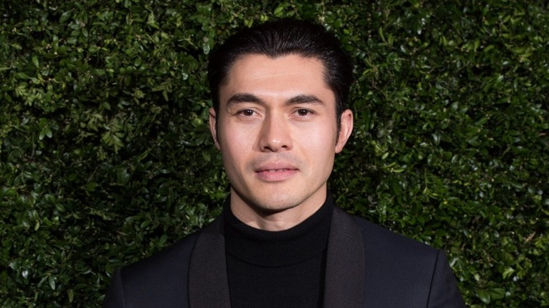 Henry Golding posing in front of bushes