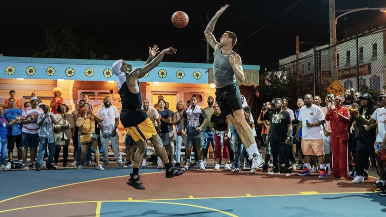 2 men playing basketball outside with people watching