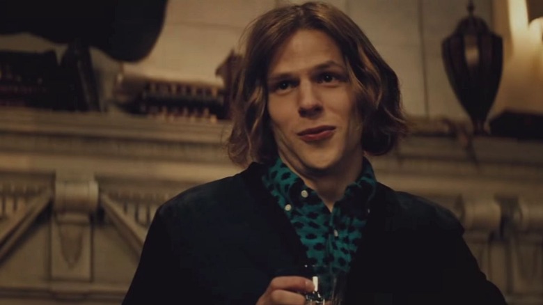 Lex Luthor holding glass and alcohol and standing by a fireplace