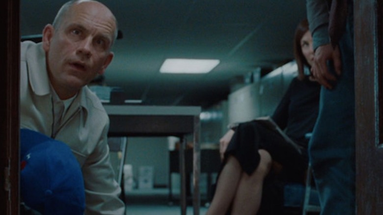 John Malkovich as himself, looking into a small doorway with surprise