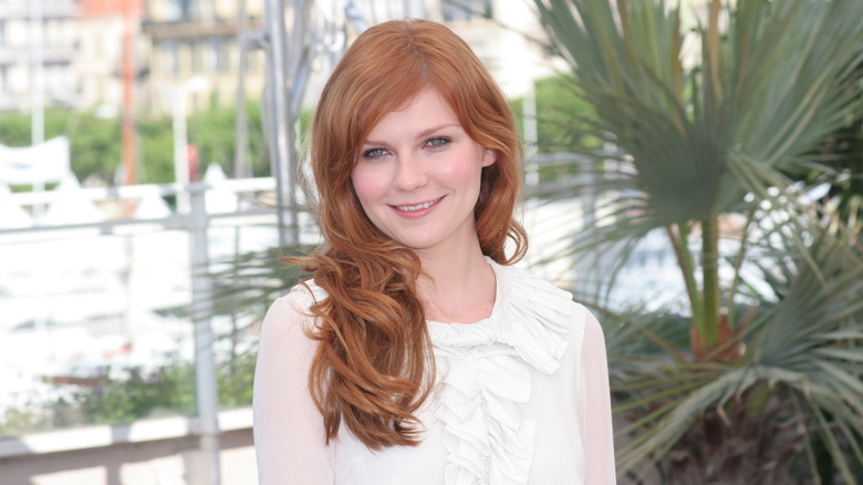 Dunst with red hair and white dress on red carpet