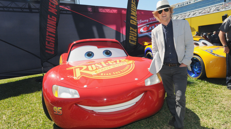 Owen Wilson stands beside Lightning McQueen